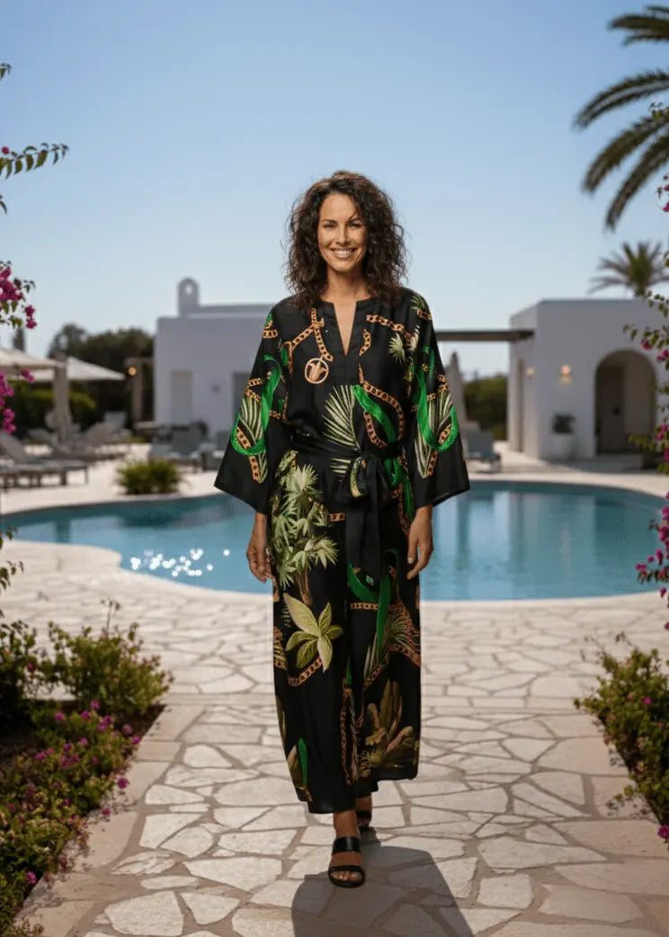 Woman in a Vicharan GOLDEN Black & Green caftan standing by a pool with palm trees and flowers aroundon greece getawy