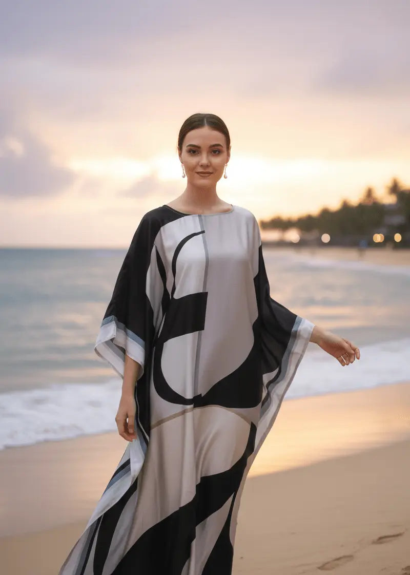 Woman in vicharan lunar grey kaftan standing on a beach at sunset.